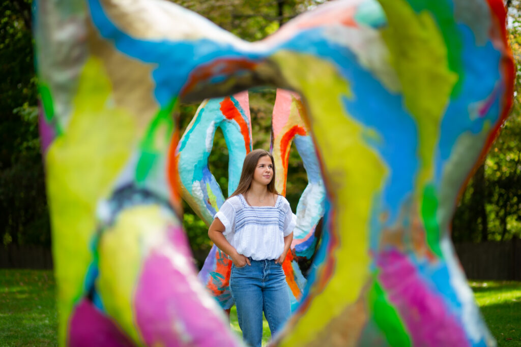Senior portrait of a girl outdoors with a colorful art sculpture. Photographed at the deCordova museum in Lincoln, Ma by Pierre Chiha Photographers