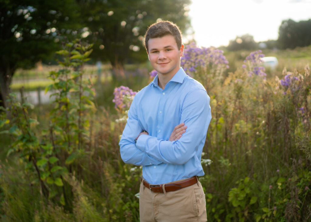 Senior portrait of a boy outdoors in nature at Great Brook Farm in Carlisle, MA. He's dressed nicely in a button down and slacks. 
