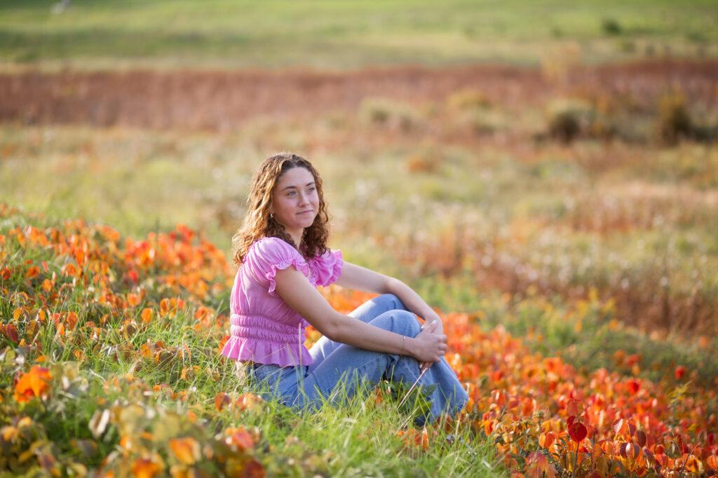 Senior portrait of a girl sitting outside in nature surrounded by flowers. Located at the Old North Bridge in Concord, MA