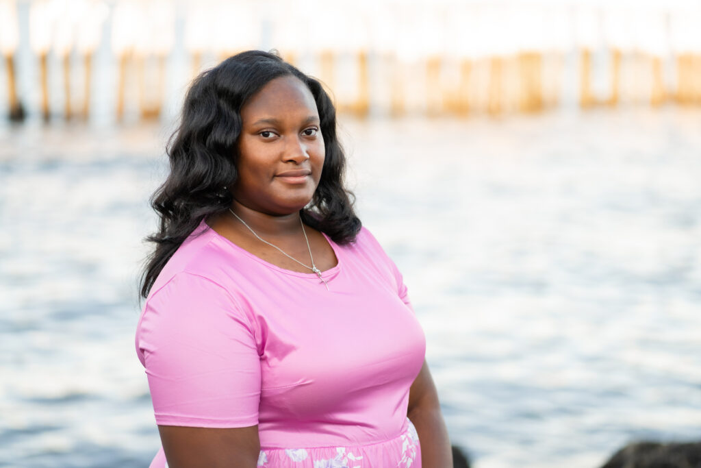 senior portrait at the beach in Boston, MA. The portrait is of a high school senior black girl wearing a pink dress. Photographed by Pierre Chiha Photographers